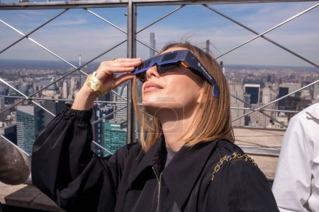 Téléchargez les photos : Solar Eclipse 2024 à New York. 08 avril 2024, New York, New York, USA : Une femme portant des lunettes de protection voit l'éclipse solaire partielle depuis le pont d'observation du 86ème étage de l'Empire State Building le 8 avril 2024 à New York - en image libre de droit