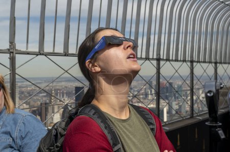 Photo for Solar Eclipse 2024 in New York City. April 08, 2024, New York, New York, USA: A woman wearing protective glasses views the partial solar eclipse from the 86th floor Observation deck of the Empire State Building on April 8, 2024 in New York City - Royalty Free Image
