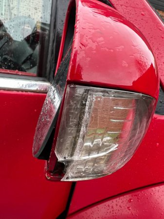 Téléchargez les photos : Close up of broken wing mirror of red car, the mirror intact, but fallen from casing and plastic unit of side light cracked on driver's side electronic mobile side mirror after collision with object - en image libre de droit