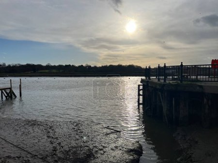 Téléchargez les photos : Beautiful sunset landscape of the water in the harbour port at Wivenhoe in Essex East Anglia England uk with sun reflected in calm estuary and boat moorings by the town edge and trees on horizon background - en image libre de droit