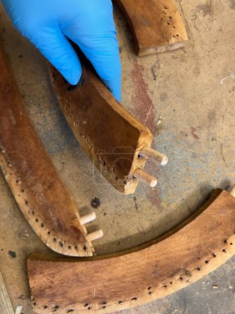 Téléchargez les photos : Close up of handmade timber frame chair in pieces being mended with new wood dowels set and glued  drill holes  re construct the vintage wood seat before upholstery craftsman hand in blue vinyl gloves - en image libre de droit