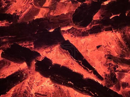 Téléchargez les photos : Gros plan du feu de cheminée des grumes de bois et des branches d'arbres brûlant avec la flamme et les braises chaudes bouillonnantes rougeoyant dans le rouge profond et l'orange contre le noir dans la nuit de jardin au printemps - en image libre de droit