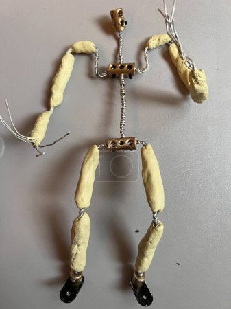 Photo for Close up of armature of single human figure headless, constructed with steel twisted wire for body arms and legs and metal bolts with animation hardening clay bones between joints built for stop motion video flat lay one colour surface background - Royalty Free Image