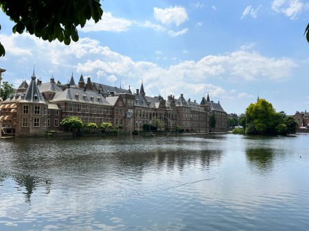 Téléchargez les photos : Paysage du bâtiment du siège du gouvernement néerlandais Le Binnenhof à La Haye Pays-Bas Hollande centre-ville regardant à travers une grande zone d'eau avec de beaux arbres et balustrade chemin de promenade Jour d'été - en image libre de droit
