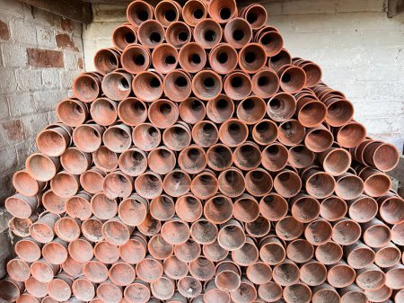 Photo for Close up of stack of old clay terracotta clay plant pots on store cupboard shelves for re use planting in brick constructed garden buildings wood shelf potting shed environment country estate Essex - Royalty Free Image