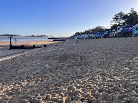 Téléchargez les photos : Beau bord de mer avec rivage sablonneux et cabanes de plage couleurs peintes sur ensoleillé Hiver froid et lumineux avec ciel bleu à Wells près de la mer à Norfolk East Anglia uk en vacances - en image libre de droit