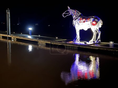 Téléchargez les photos : Paysage du Souvenir Dimanche Statue illuminée du cheval avec des coquelicots la nuit la lumière bleue rouge blanche reflétée dans l'eau du port Novembre soir sombre à Wells Prochain la mer Norfolk East Anglia UK - en image libre de droit