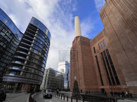 Téléchargez les photos : Londres Angleterre Royaume-Uni - 31 décembre 2023 : Développement de la centrale électrique de Battersea avec les tours principales du bâtiment d'origine rénové et la fenêtre du bloc de bureaux avec fond bleu ciel - en image libre de droit