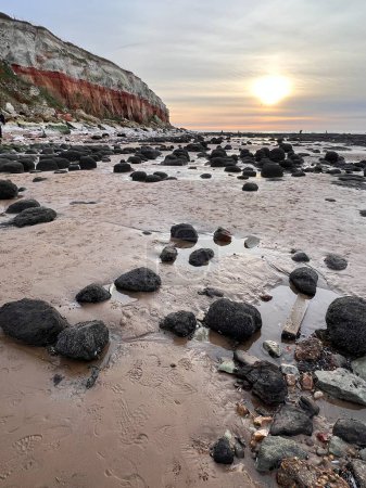 Téléchargez les photos : Belle plage de coucher de soleil paysage de la falaise jurassique plage de sable à Hunstanton Norfolk uk en début de soirée lumière faible soleil dans le ciel coloré réfléchi sur le rivage de sable rocheux par l'océan de la mer au printemps - en image libre de droit