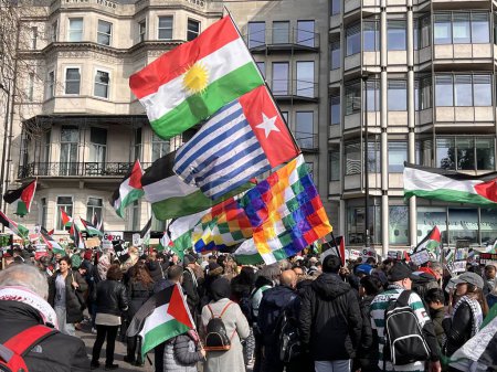 Photo for London, England, UK - March 9 2024: colourful flags and crowds at peaceful anti- war coalition protest from Hyde Park to US embassy for ceasefire in Gaza Middle East groups include Muslims Jews Christians marching chanting buildings under blue sky - Royalty Free Image