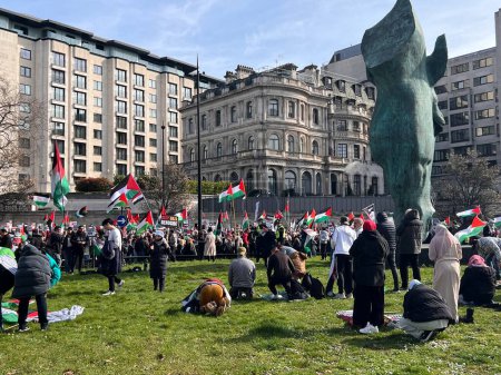 Photo for Muslims praying on grass in London, England, UK - March 9 2024 at peaceful anti- war coalition protest for ceasefire in Gaza Middle East from Hyde Park to US embassy groups include Muslims Jews Christians marching and chanting with flags and banners - Royalty Free Image