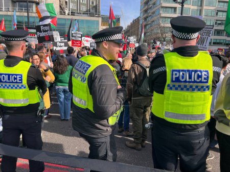 Photo for London, England, UK - March 9 2024: Police guarding peaceful anti- war coalition protest demonstration Hyde Park to US embassy for ceasefire in Gaza Middle East groups include Muslims Jews Christians march colourful  flags banners by Wellington arch - Royalty Free Image
