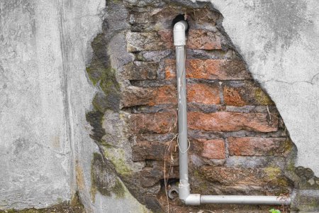Photo for Broken concrete wall revealing red brick and water piping - Royalty Free Image