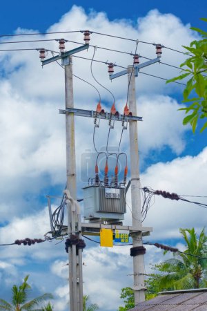 Photo for Electrical transformer power box on metal poles with wires in Bali, Indonesia. Blue sky and white clouds background. - Royalty Free Image