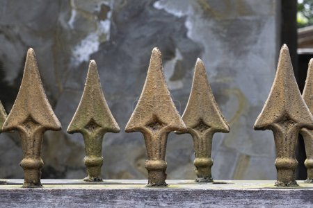 Close up view group of large brass spear finials with focus on foreground ones on top of iron gate.