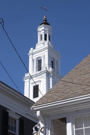 View of church's white steeple in background of shingle roof and royal blue sky