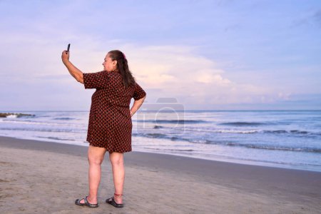 Beautiful woman standing on the beach taking a selfie by the sea in Cartagena de Indias, Colombia.