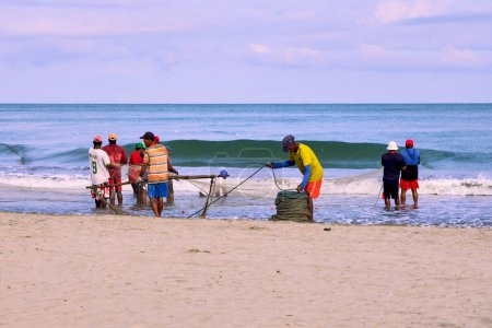 Foto de Cartagena, Bolívar Colombia - 1 de febrero de 2024: Los pescadores terminan de enrollar las cuerdas con las que arrastran la red de tranvía con los peces recogidos en las playas de Cartagena de Indias, Colombia. - Imagen libre de derechos