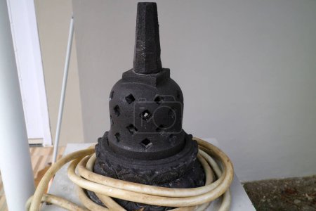 a photo of an artificial stupa made of cement. For outdoor decoration. black, with a water hose wrapped around it