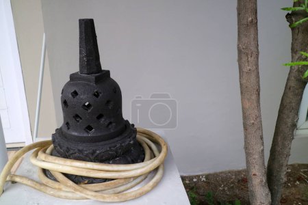 a photo of an artificial stupa made of cement. For outdoor decoration. black, with a water hose wrapped around it