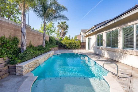 Photo for A beautiful blue pool in a residential backyard surrounded by large palm trees and a blue sky. Great for designers and virtual staging - Royalty Free Image