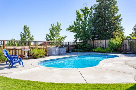 Una piscina en un patio residencial con sillas azules, árboles verdes y un cielo azul. Ideal para la puesta en escena virtual