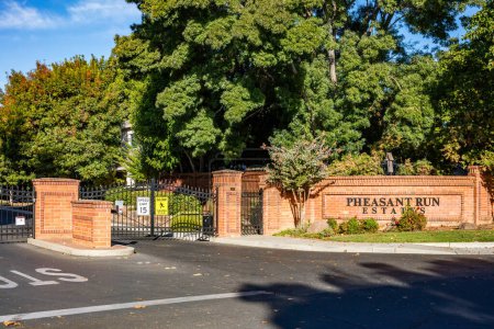Photo for Brentwood, California October 20, 2023: Pheasant Run Estates entrance in Brentwood, California with a gate, green trees and a brick wall - Royalty Free Image