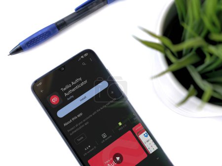 Foto de Lod, Israel - July 16,2023: Modern workspace with smartphone with Twilio Authy Authenticator app play store page on white background. Close up top view flat lay. - Imagen libre de derechos