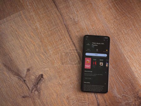 Foto de Lod, Israel - July 16,2023: TIDAL Music app play store page on smartphone on wooden background. Top view flat lay with copy space. - Imagen libre de derechos