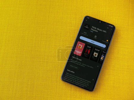 Foto de Lod, Israel - July 16,2023: TIDAL Music app play store page on smartphone on a yellow fabric background. Top view flat lay with copy space. - Imagen libre de derechos