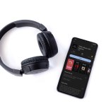 Lod, Israel - July 16,2023: Smartphone with TIDAL Music app play store page and wireless headphones on white background. Top view flat lay with copy space.