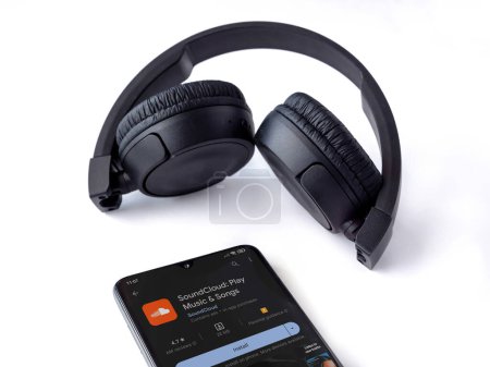 Photo for Lod, Israel - July 16,2023: Smartphone with SoundCloud app play store page and wireless headphones on white background. Top view flat lay with copy space. - Royalty Free Image