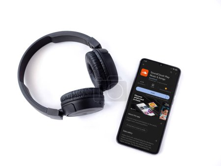 Foto de Lod, Israel - July 16,2023: Smartphone with SoundCloud app play store page and wireless headphones on white background. Top view flat lay with copy space. - Imagen libre de derechos