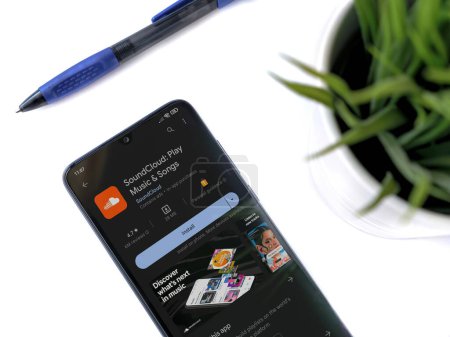 Foto de Lod, Israel - July 16,2023: Modern workspace with smartphone with SoundCloud app play store page on white background. Close up top view flat lay. - Imagen libre de derechos