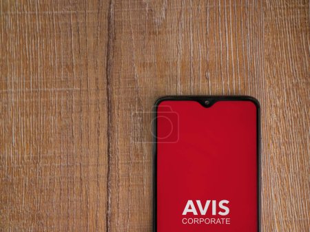 Photo for Lod, Israel - July 16,2023: Avis Corporate app launch screen on smartphone on wooden background. Top view flat lay with copy space. - Royalty Free Image