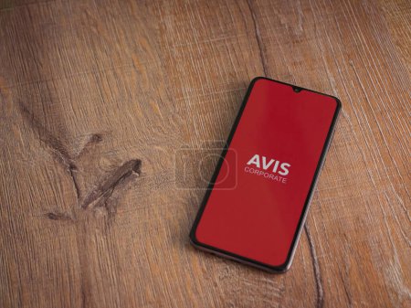 Photo for Lod, Israel - July 16,2023: Avis Corporate app launch screen on smartphone on wooden background. Top view flat lay with copy space. - Royalty Free Image