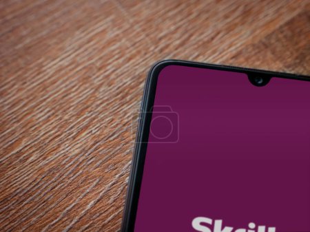 Photo for Lod, Israel - July 16,2023: Skrill app launch screen on smartphone on wooden background. Top view flat lay with copy space. - Royalty Free Image