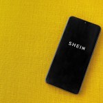 Lod, Israel - July 16,2023: Shein app launch screen on smartphone on yellow fabric background. Top view flat lay with copy space.