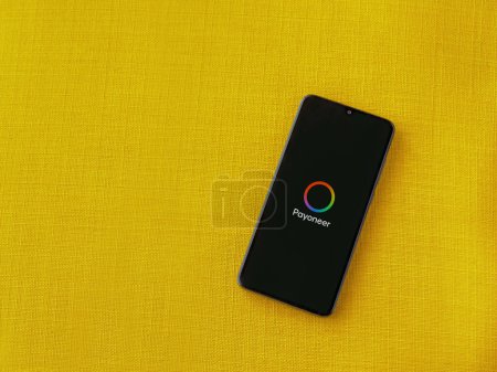Photo for Lod, Israel - July 16,2023: Payoneer app launch screen on smartphone on yellow fabric background. Top view flat lay with copy space. - Royalty Free Image