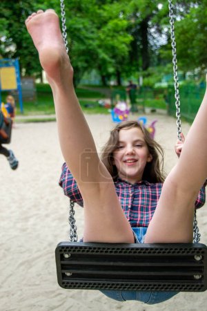 Close up happy little child girl play and sitting on the swing in the nature park. Teen girl on a swing in the summer park. High quality photo