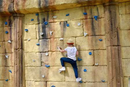 Foto de El chico se dedica a escalar rocas. Arnés de escalada equipo deportivo de seguridad. Parque de la ciudad de atracciones de cuerda, carrera de obstáculos. Centro de atracción infantil para niños. Foto de alta calidad - Imagen libre de derechos