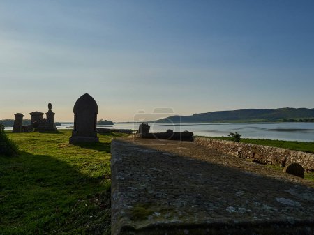 Foto de Kinross, Escocia - 05 21 2018: Cementerio de Kinross con antiguos edificios históricos y lápidas en la orilla del lago Loch leven en Escocia, Reino Unido. - Imagen libre de derechos
