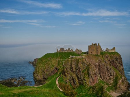 Photo for Dunnattor Castle, Scotland - 05 21 2018: Dunnottar Castle sitting high on a steep cliff of the atlantic ocean coastline of Scotland on a sunny day with yellow gorse. - Royalty Free Image