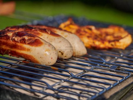 Foto de Salchicha de cerdo alemana bratwurst cocinar en una parrilla de barbacoa sobre carbón vegetal abierto en las tierras altas escocesas en un día soleado. - Imagen libre de derechos