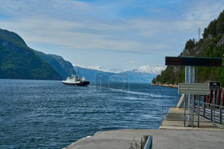 typical norwegian car ferry crossing a beautiful fjord between the mountains transporting passengers and cars on the way to Geiranger on a sunny day,