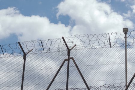 High wire fence with barbed wire against blue sky background. Border, protection zone.