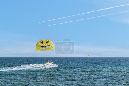 Photo for Parasailing in the sea. Flight to parachute. A yellow parasail parachute with a smiley face being pulled by a motorboat. - Royalty Free Image