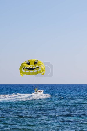 Photo for Parasailing in the sea. Yellow parachute with smiley face on sky background. Flying parachute with a smiley face. - Royalty Free Image