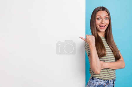 Photo of positive impressed woman with long hairstyle wear striped t-shirt directing empty space isolated on blue color background.