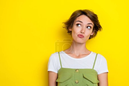 Photo of adorable gorgeous thoughtful girl with bob hairdo wear white t-shirt look empty space isolated on yellow color background.